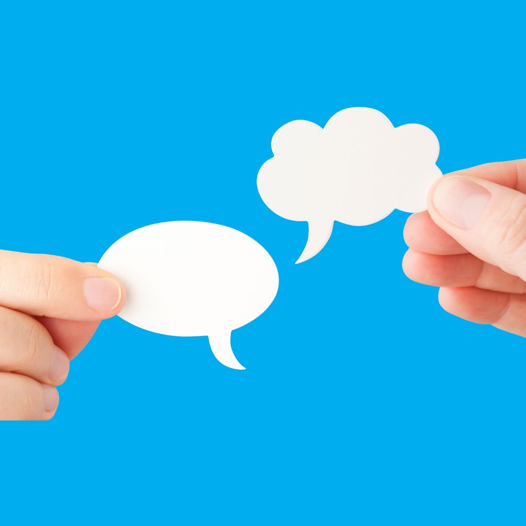 communication-change-leadership Close up photo showing two hands holding up paper speech bubbles against a blue background.